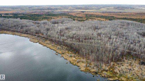 Expansive aerial overview showcasing a serene body of water, dense woodland, and a distant treeline - Rge Rd 62, Rural Barrhead County, AB 