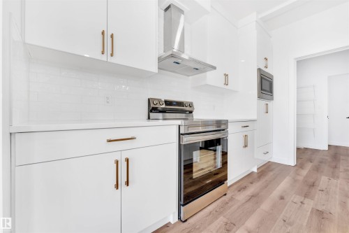 Modern kitchen featuring stainless steel appliances, white flat-panel cabinetry with bronze hardware, a subway tile backsplash, and light wood-finish flooring - 523 Kleins Court, Leduc, AB - Indoor Photo Showing Kitchen