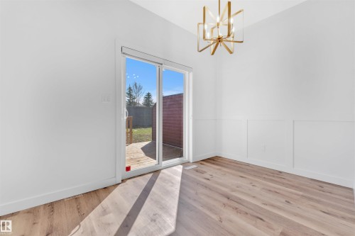 Spacious room featuring wood-finish flooring, white walls with wainscoting, and a modern gold-toned geometric chandelier - 523 Kleins Court, Leduc, AB - Indoor Photo Showing Other Room