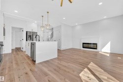 Open-concept living space featuring wood-finish flooring, a contemporary kitchen island with pendant lighting, stainless steel appliances, and a modern fireplace - 