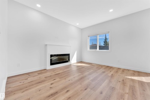 Bright room with wood-finish flooring, recessed lighting, a modern built-in fireplace, and a large window with white trim - 523 Kleins Court, Leduc, AB - Indoor Photo Showing Living Room With Fireplace