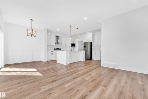 Open-concept living space featuring wood-finish flooring, a contemporary kitchen with white cabinetry, stainless steel appliances, and a central island - 523 Kleins Court, Leduc, AB - Indoor Photo Showing Kitchen