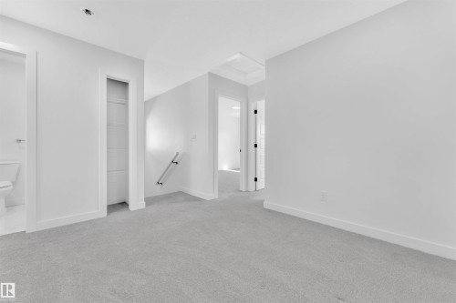 Carpeted hallway with white walls and trim, featuring a built-in shelving unit, a partial view of a toilet, and multiple doorways with dark hardware - 523 Kleins Court, Leduc, AB - Indoor Photo Showing Other Room