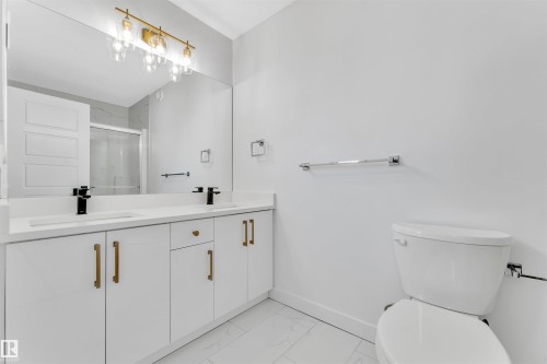 Spacious bathroom featuring a dual vanity with white cabinetry, gold-finish hardware, and a large mirror - 523 Kleins Court, Leduc, AB - Indoor Photo Showing Bathroom
