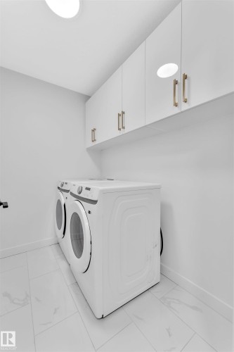 Contemporary laundry space featuring white flat-panel cabinetry with gold-finish hardware, a pair of full-size front-loading machines, and light-toned tile flooring - 523 Kleins Court, Leduc, AB - Indoor Photo Showing Laundry Room