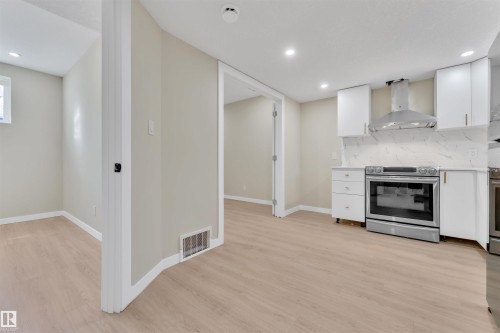 Kitchen area featuring light wood-finish flooring, white cabinetry with gold-tone pulls, stainless steel appliances, and a white marble-look backsplash - 523 Kleins Court, Leduc, AB - Indoor