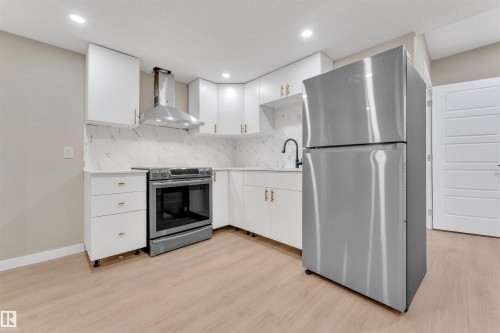 Kitchen featuring white cabinetry with gold-finish hardware, stainless steel appliances, a white patterned backsplash, and light wood-finish flooring - 523 Kleins Court, Leduc, AB - Indoor Photo Showing Kitchen