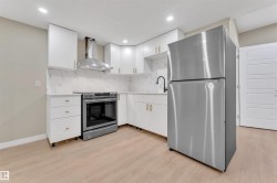 Kitchen featuring white cabinetry with gold-finish hardware, stainless steel appliances, a white patterned backsplash, and light wood-finish flooring - 