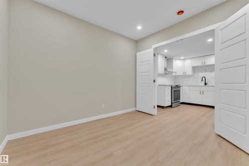 Light wood-finish flooring extending into a modern kitchen with white cabinetry, a white marble-patterned backsplash, and stainless steel appliances - 523 Kleins Court, Leduc, AB - Indoor Photo Showing Kitchen