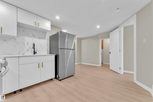 Compact kitchen area featuring white cabinetry, gold-tone hardware, and a white marble-patterned backsplash - 523 Kleins Court, Leduc, AB - Indoor