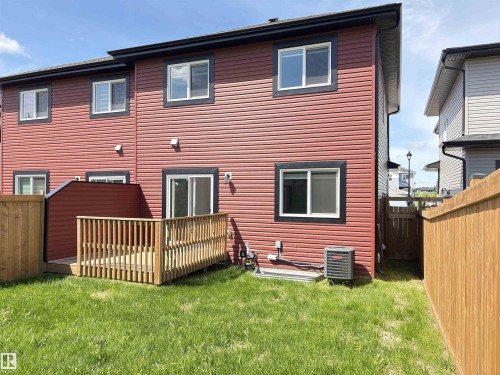 Rear exterior featuring red siding with black trim, a wood deck, a sliding glass door, multiple windows, and a grassy area - 523 Kleins Court, Leduc, AB - Outdoor With Exterior