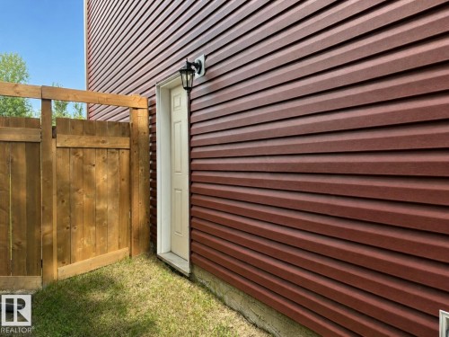 Red horizontal siding with a light-colored exterior door and a black wall-mounted lantern - 523 Kleins Court, Leduc, AB - Outdoor With Exterior