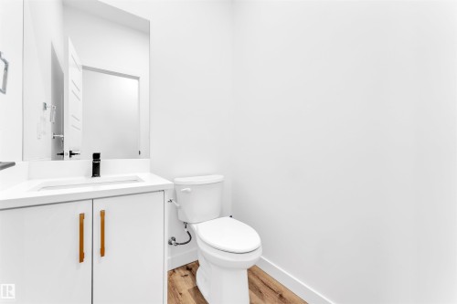 Modern bathroom featuring a white vanity with linear wood-finish pulls, a rectangular undermount sink, a matte black single-handle faucet, and wood-finish flooring - 523 Kleins Court, Leduc, AB - Indoor Photo Showing Bathroom