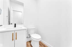 Modern bathroom featuring a white vanity with linear wood-finish pulls, a rectangular undermount sink, a matte black single-handle faucet, and wood-finish flooring - 