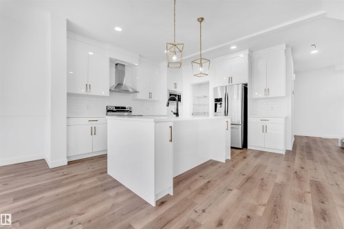 Bright kitchen featuring white cabinetry, a large central island, stainless steel appliances, wood-finish flooring, and two modern pendant lights - 523 Kleins Court, Leduc, AB - Indoor Photo Showing Kitchen With Upgraded Kitchen