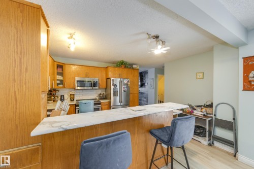 Kitchen featuring wood cabinetry, stainless steel appliances, a white subway tile backsplash, and a breakfast bar with a stone-finish countertop - 17328 106 Street, Edmonton, AB 