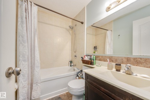 Bathroom featuring a white bathtub, ceramic tile shower surround, single vanity with integrated sink, and a large wall-mounted mirror - 17328 106 Street, Edmonton, AB 
