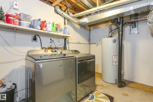 Dedicated laundry space featuring a side-by-side washer and dryer, an exposed ceiling with ductwork, a wall-mounted shelf, and a water heater - 17328 106 Street, Edmonton, AB 