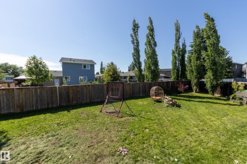 Expansive backyard featuring a manicured lawn, full wood privacy fencing, and mature trees providing natural screening - 17328 106 Street, Edmonton, AB 
