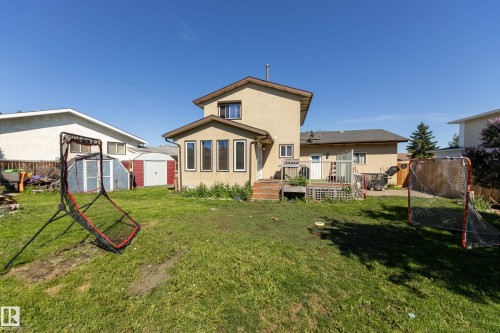 Spacious backyard with a grass lawn, featuring a multi-level deck, stucco exterior, and an additional storage shed - 17328 106 Street, Edmonton, AB 