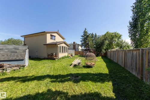 Expansive grassy backyard featuring a full-height wooden privacy fence, mature trees, and a detached shed with an asphalt shingle roof - 17328 106 Street, Edmonton, AB 
