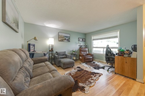 Spacious living area featuring wood-finish flooring, light blue wall paint, and a large window with blinds - 17328 106 Street, Edmonton, AB 