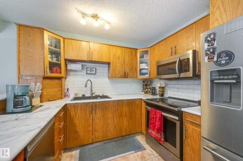 Kitchen featuring wood cabinetry, white subway tile backsplash, and white marble-look countertops - 17328 106 Street, Edmonton, AB 