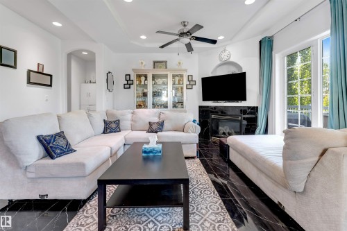 Living area featuring black tile flooring, a built-in fireplace with a dark surround, a ceiling fan with integrated lighting, and recessed ceiling lights - 7920 7 Avenue, Edmonton, AB 