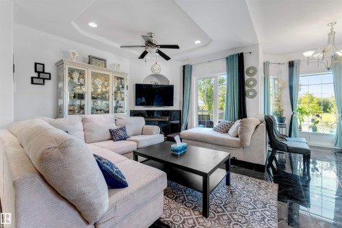 Spacious living area featuring polished black tile flooring, a tray ceiling with a ceiling fan, and large windows with transom details - 7920 7 Avenue, Edmonton, AB 