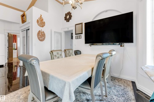 Dining area featuring high ceilings with gold-toned trim, a wall-mounted flat-screen display, and black polished tile flooring - 7920 7 Avenue, Edmonton, AB 