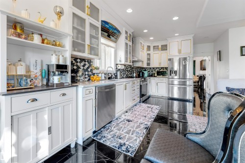 Modern kitchen featuring white cabinetry, stainless steel appliances, black tile flooring, a detailed tile backsplash, and quartz countertops - 7920 7 Avenue, Edmonton, AB 
