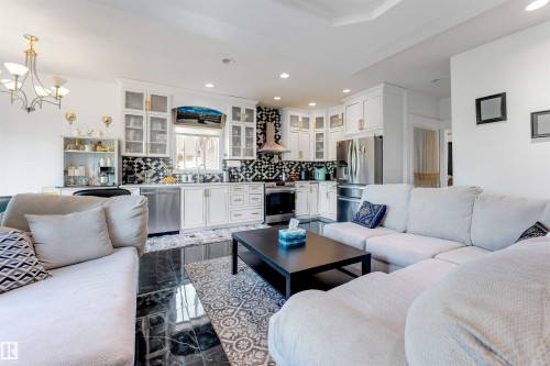 Open-concept living space featuring a kitchen with white cabinetry, black and white mosaic tile backsplash, stainless steel appliances, and a stainless steel range hood - 7920 7 Avenue, Edmonton, AB 