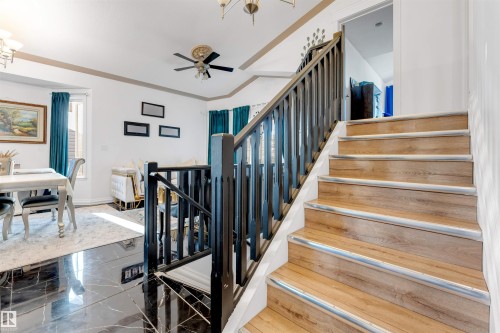 Hardwood staircase with dark wood-finish balusters, complemented by polished black tile flooring and a neutral wall palette - 7920 7 Avenue, Edmonton, AB 