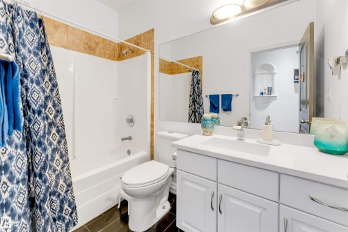 Full bathroom featuring a white vanity with integrated sink, a large wall-mounted mirror, a white toilet, and a shower-tub combination with tile surround - 7920 7 Avenue, Edmonton, AB 