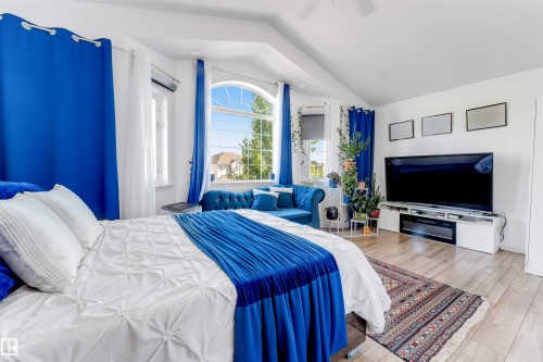 Spacious room featuring vaulted ceilings, light wood-finish flooring, and a floor-to-ceiling arched window - 7920 7 Avenue, Edmonton, AB 