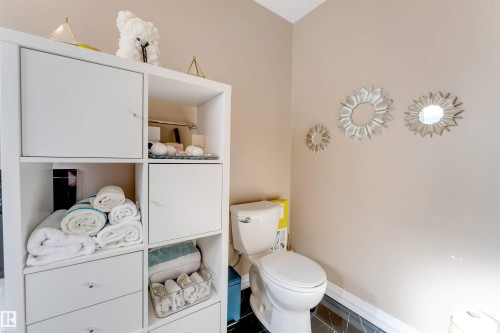 White storage unit with open shelving and cabinet doors, a standard toilet, and dark-toned floor tiling - 7920 7 Avenue, Edmonton, AB 