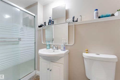 Bathroom featuring a white pedestal sink vanity, framed mirror, and a shower with frosted glass sliding doors - 7920 7 Avenue, Edmonton, AB 