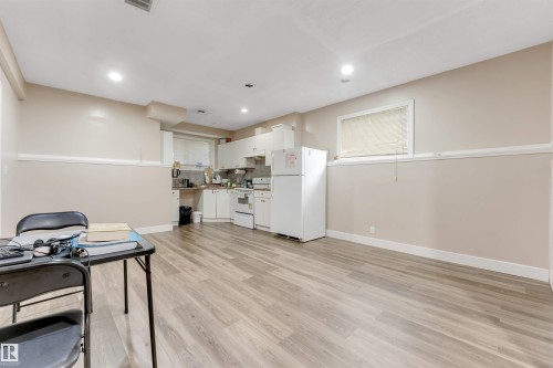 Open-concept living area featuring wood-finish flooring, recessed lighting, and a functional kitchen with white cabinetry and appliances - 7920 7 Avenue, Edmonton, AB 