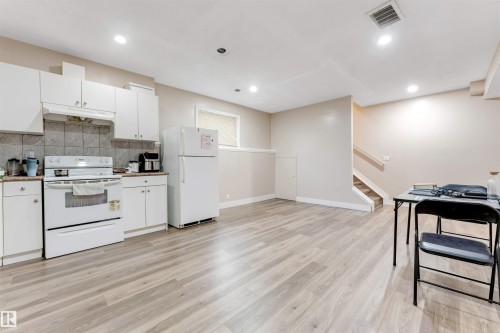 Spacious open-concept room featuring wood-finish flooring, white cabinetry, and a tile backsplash - 7920 7 Avenue, Edmonton, AB 