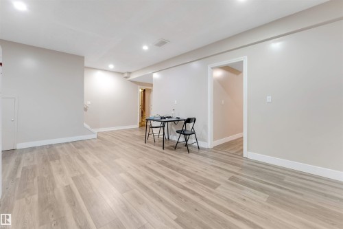 Spacious room featuring light wood-finish flooring, recessed lighting, neutral wall paint, white baseboards, and a doorway leading to an interior area - 7920 7 Avenue, Edmonton, AB 