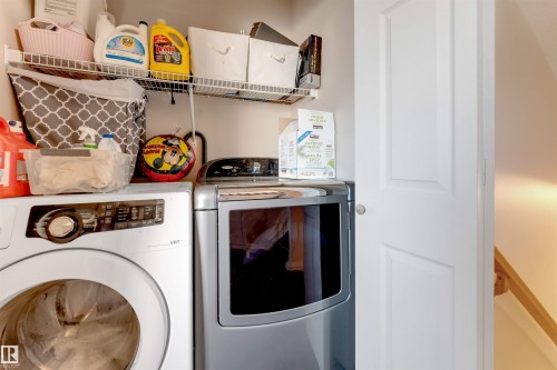 Dedicated laundry area featuring a front-load washer and dryer set, overhead wire shelving, and a paneled white door - 7920 7 Avenue, Edmonton, AB 