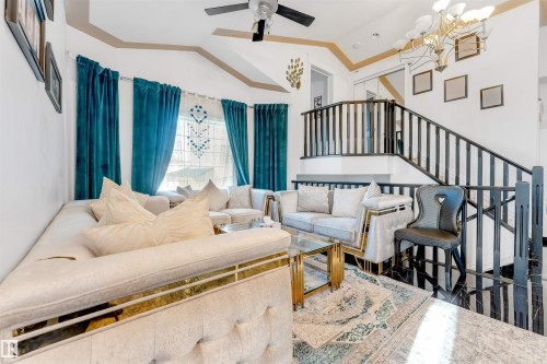 Two-story living area featuring a staircase with black railings, high vaulted ceilings, large windows, and a multi-arm chandelier - 7920 7 Avenue, Edmonton, AB 