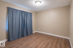 Neutral-toned walls complement wood-finish flooring in this room featuring a window with blue drapes, white baseboards, and a ceiling-mounted light fixture - 