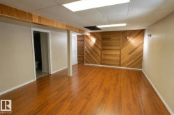Spacious room featuring wood-finish flooring, a decorative wood accent wall with diagonal paneling, and two wall-mounted lights - 