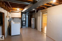 Utility area featuring exposed wood ceiling joists and ductwork, a laundry appliance, a furnace unit, and a water heater - 