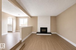 Living area featuring wood-finish flooring, a white brick fireplace with a black hearth, and neutral wall tones - 