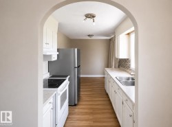 Kitchen featuring an arched entryway, white cabinetry, a tiled backsplash, wood-finish flooring, and stainless steel appliances that bring you into the dining room. - 
