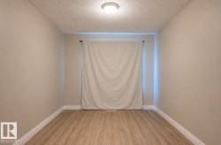Spacious room featuring wood-finish flooring, neutral-toned walls, a ceiling-mounted light fixture, and white baseboards - 