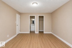Spacious room featuring wood-finish flooring, neutral-toned walls, a ceiling-mounted light fixture, and white baseboards - 