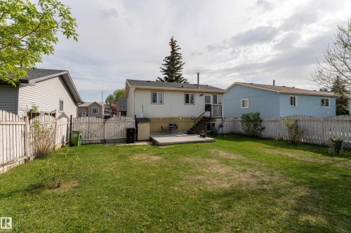 Expansive fenced backyard featuring a wood fence, concrete patio, exterior deck with stairs, and mature trees - 4620 37A Avenue, Edmonton, AB - Outdoor With Backyard